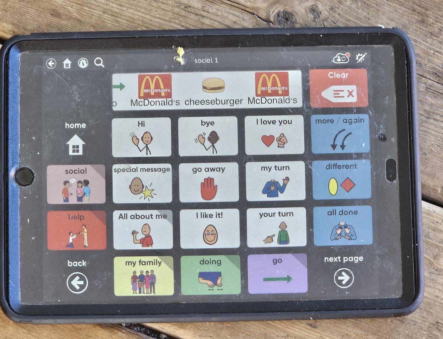 Jimmy's AAC device screen displaying a communication page with large, colorful icons. The selected message reads 'McDonald's cheeseburger McDonald's,' showing that Jimmy independently navigated and chose specific food-related phrases to express his thoughts.